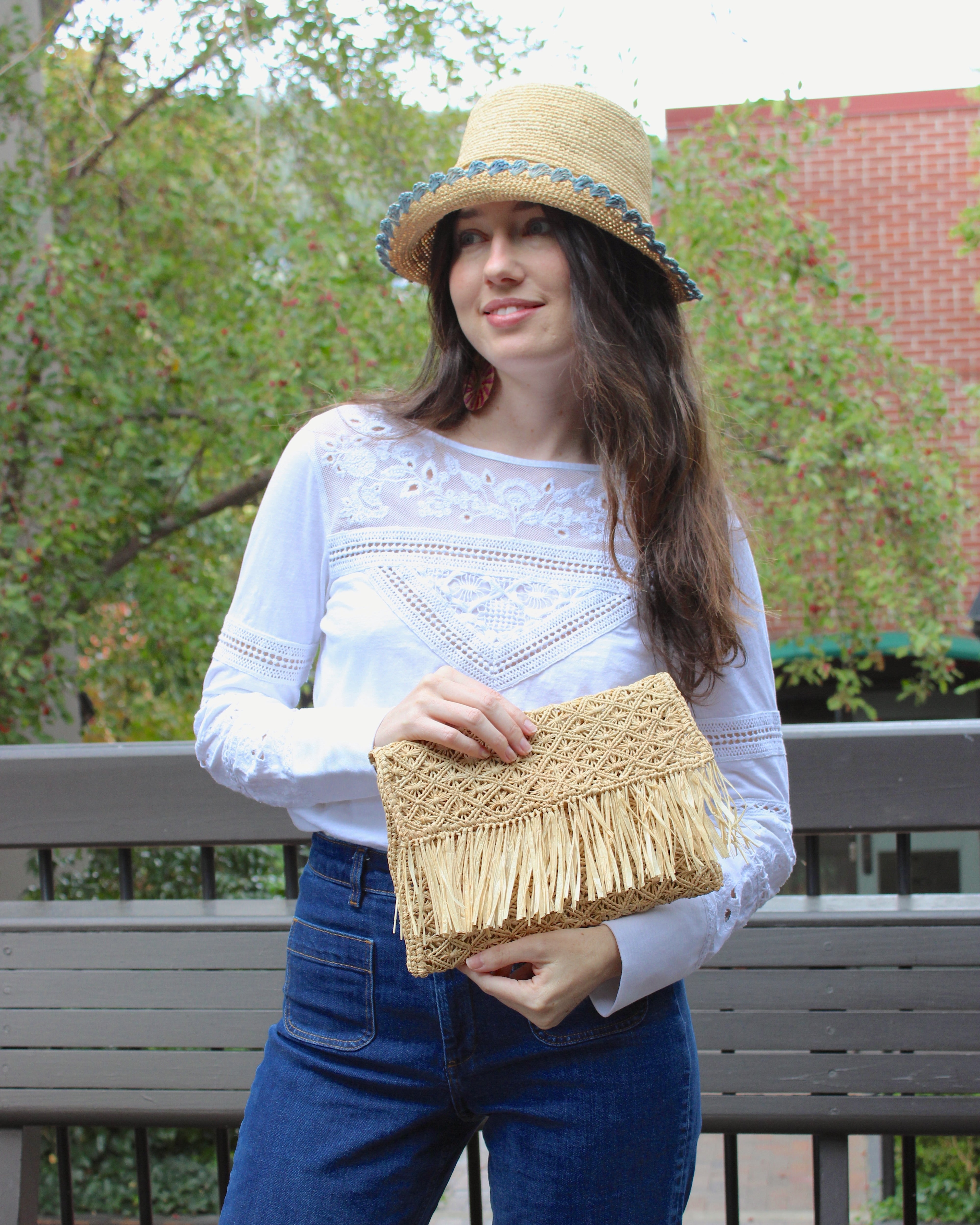 Model wearing Luli Macrame Diamond and Crochet Straw Envelope Clutch Purse with Raw Fringe Trim Edge handmade macrame and crochet natural raffia palm fiber in a solid hue of natural straw color in a diagonal geometric pattern of starburst or flower inside diamonds with hand brushed raw fringe trim edge along the top flap of the envelope design handbag  - Shebobo (with Kate 3" Brim Crochet Bucket Straw Hats with Colored Lace Weave Edge)