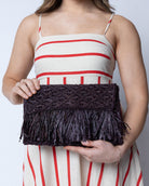 Model wearing Luli Macrame Diamond and Crochet Straw Envelope Clutch Purse with Raw Fringe Trim Edge handmade macrame and crochet natural raffia palm fiber in a solid hue of Mocha dark/chocolate/brown in a diagonal geometric pattern of starburst or flower inside diamonds with hand brushed raw fringe trim edge along the top flap of the envelope design handbag  - Shebobo