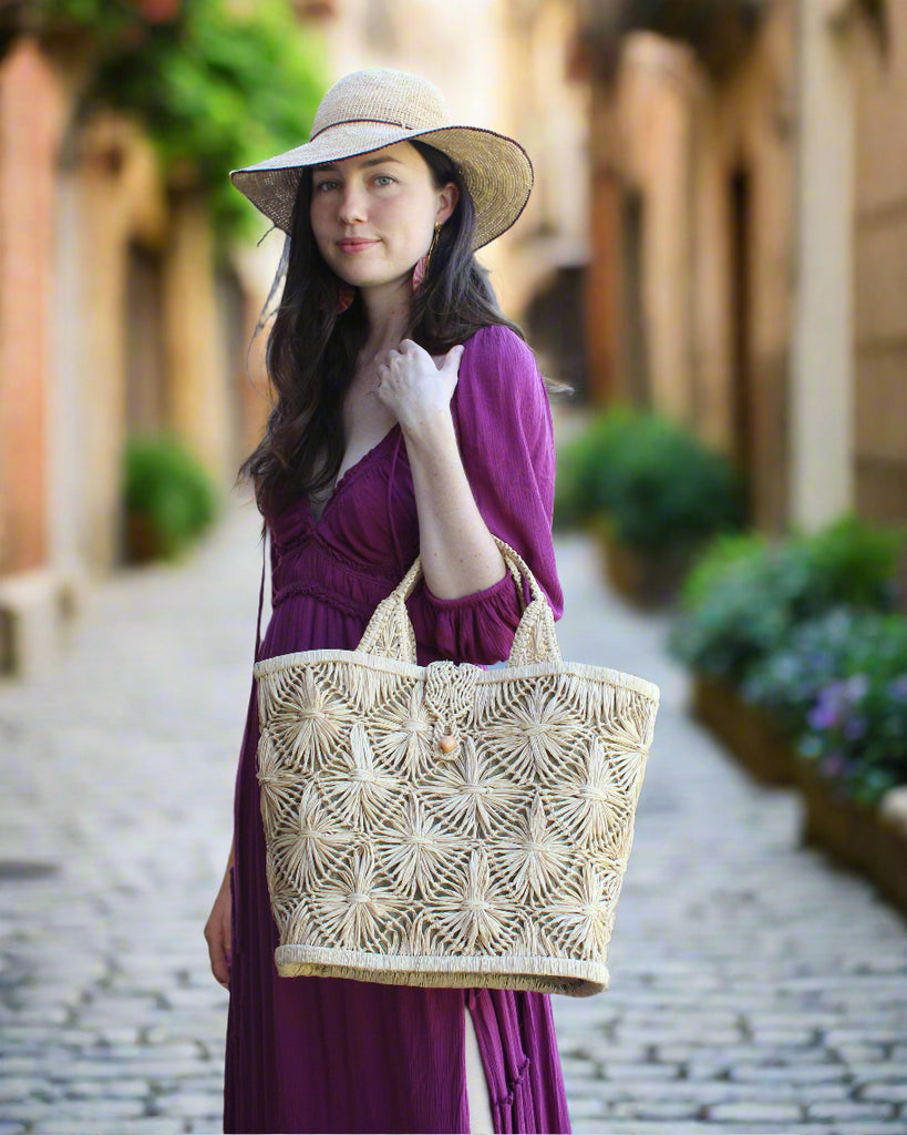 Model wearing Lusha Macrame Diamond and Crochet Straw Basket Bag handmade natural raffia palm fiber in a solid hue of natural straw color macrame into a large geometric diagonal diamond pattern with loop banding on the top and bottom edges, macrame diamond and loop handles, with knotted matching flap closure beach bag shoulder bag purse - Shebobo (with Rachel 4" Brim Crochet Straw Sun Hats with Colored Edge)