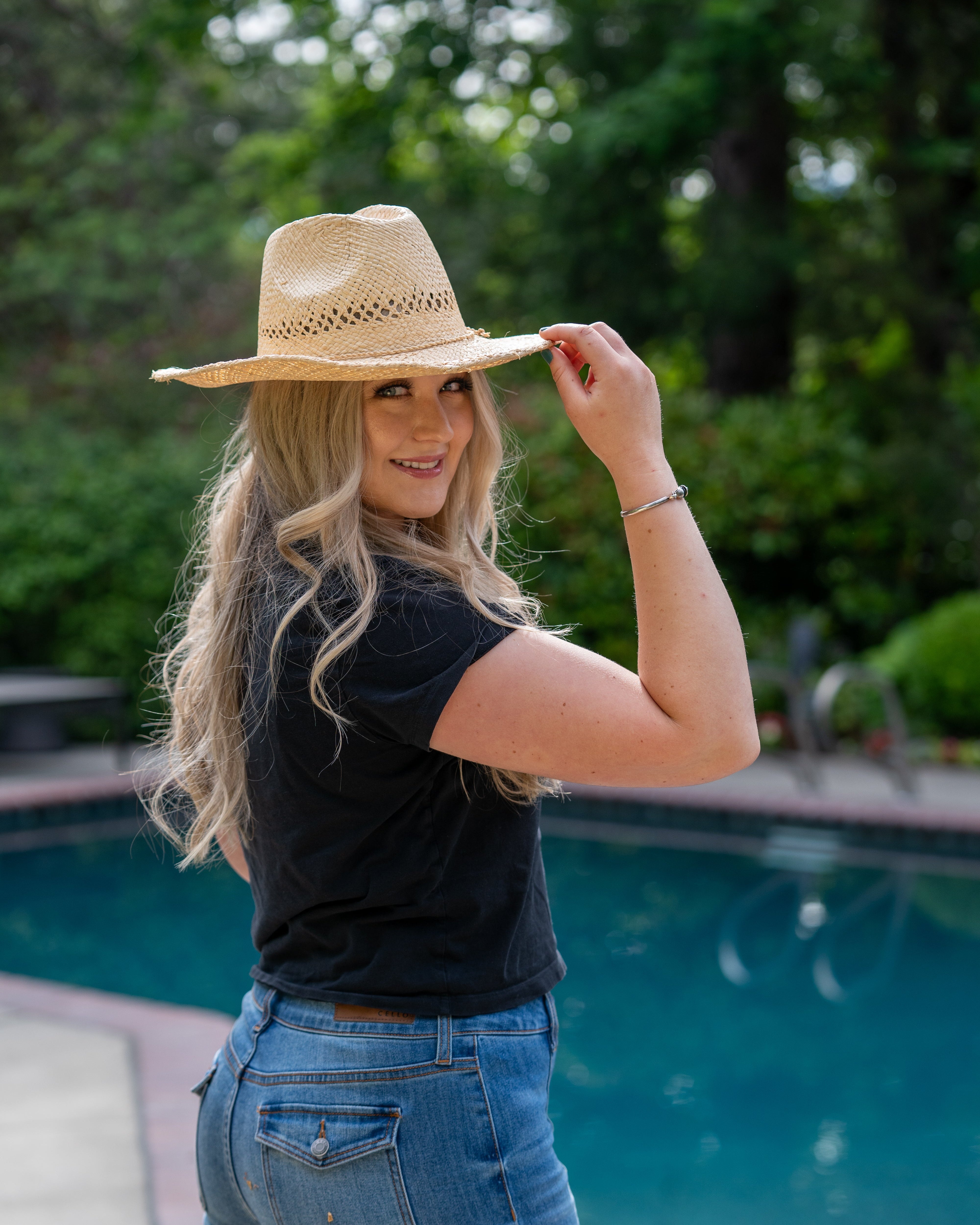 Model wearing Macho Natural Unisex Straw Cowboy Hat with Adjustable Wire Rim handmade woven raffia in a solid hue of natural straw color in a structured crown style with open weave pattern for breathability and pliable wire rim with matching twisted cord hat band - Shebobo