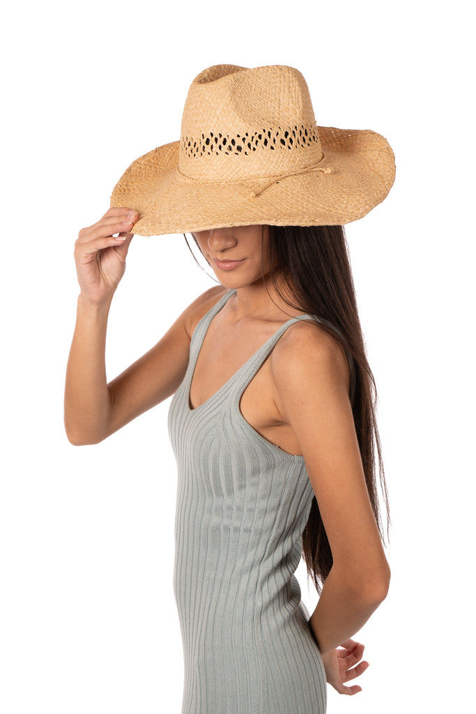 Model wearing Macho Natural Unisex Straw Cowboy Hat with Adjustable Wire Rim handmade woven raffia in a solid hue of natural straw color in a structured crown style with negative space for breathability and pliable wire rim with matching twisted cord hat band - Shebobo