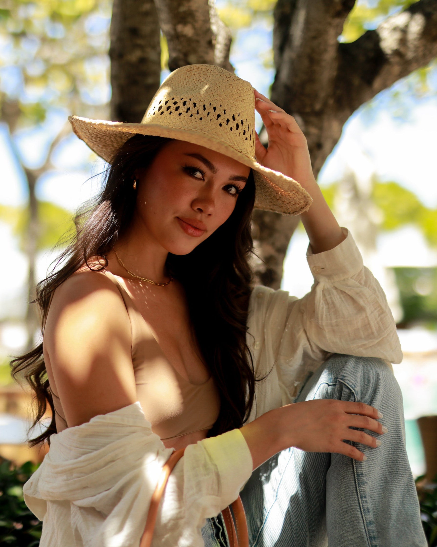 Model wearing Macho Natural Unisex Straw Cowboy Hat with Adjustable Wire Rim handmade woven raffia in a solid hue of natural straw color in a structured crown style with negative space for breathability and pliable wire rim with matching twisted cord hat band - Shebobo