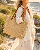 Model wearing Madeline Natural XL Crochet Raffia Straw Basket Shoulder Bag with Pockets handmade raffia palm fiber in a solid hue of natural straw color with crochet horizontal subtle band texture, round boucle nub edges, oversized external pockets, and leather handles - Shebobo