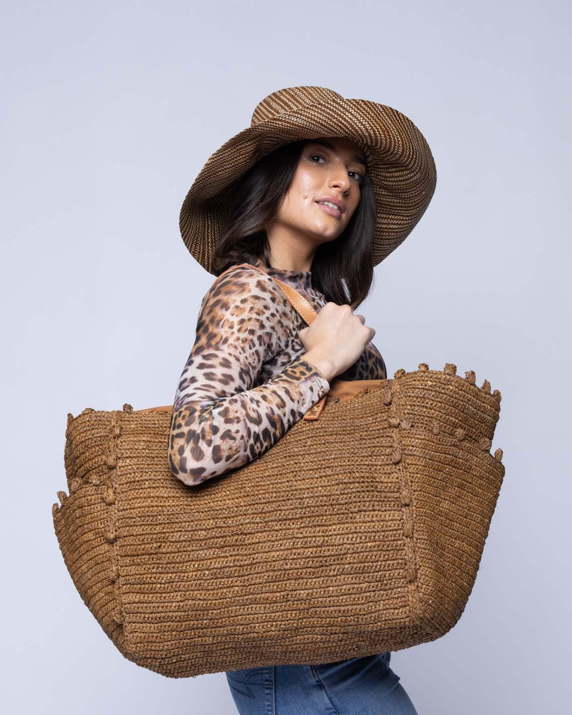 Model wearing Side view Madeline Tobacco XL Crochet Raffia Straw Basket Shoulder Bag with Pockets handmade raffia palm fiber in a solid hue of tobacco dark/cinnamon/brown with crochet horizontal subtle band texture, round boucle nub edges, oversized external pockets, and leather handles - Shebobo