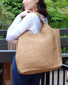 Model wearing Mamie XL Crochet Straw Basket Handbag handmade crochet natural raffia palm fiber in a solid hue of cappuccino tea/light/brown purse beach bag - Shebobo