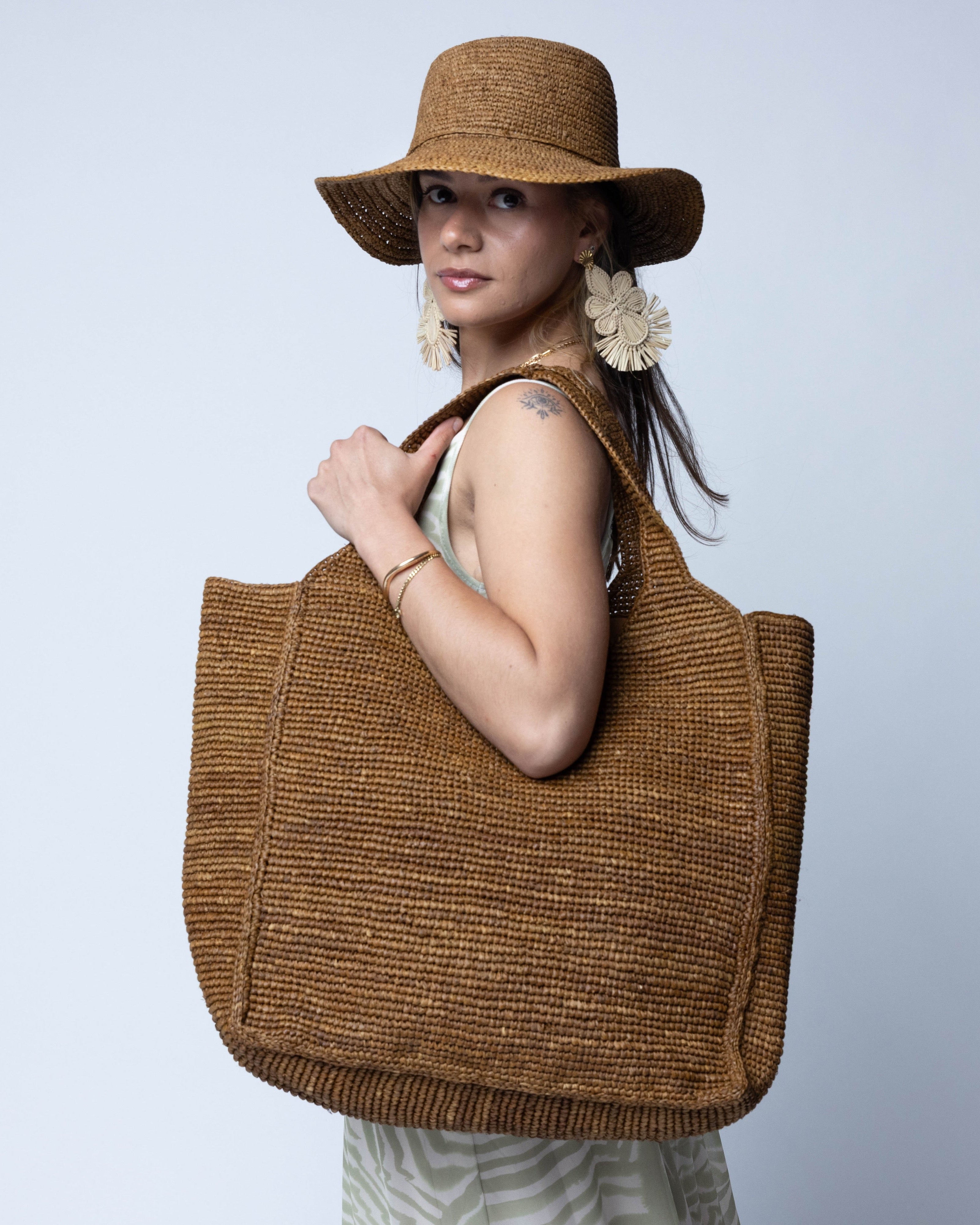 Model wearing Mamie XL Crochet Straw Basket Handbag handmade crochet natural raffia palm fiber in a solid hue of Tobacco cinnamon/dark/brown purse beach bag - Shebobo (with Bolero 3" Brim Crochet Straw Sun Hats)