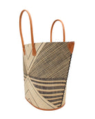 Side view Mariposa Large Straw Tote Bag handmade loomed natural raffia palm fiber in a multi paneled pattern design of pinstripe, melange, and wide stripe combinations geometrically radiating from the center point of the bag outwards in a two tone color combination of Natural straw color and black with a solid hue of color on the back of the bag plus leather handles and embellishments shoulder bag - Shebobo