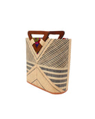 Side view Mariposa Zuki Raffia Straw Bucket Handbag with Wood Triangle Handles  handmade loomed raffia palm fiber in a multi paneled pattern design of pinstripe, melange, and wide stripe combinations geometrically radiating from the center point of the bag outwards in a two tone color combination of Natural straw color and black with a solid hue of color on the back of the bag plus carved wooden handles purse - Shebobo