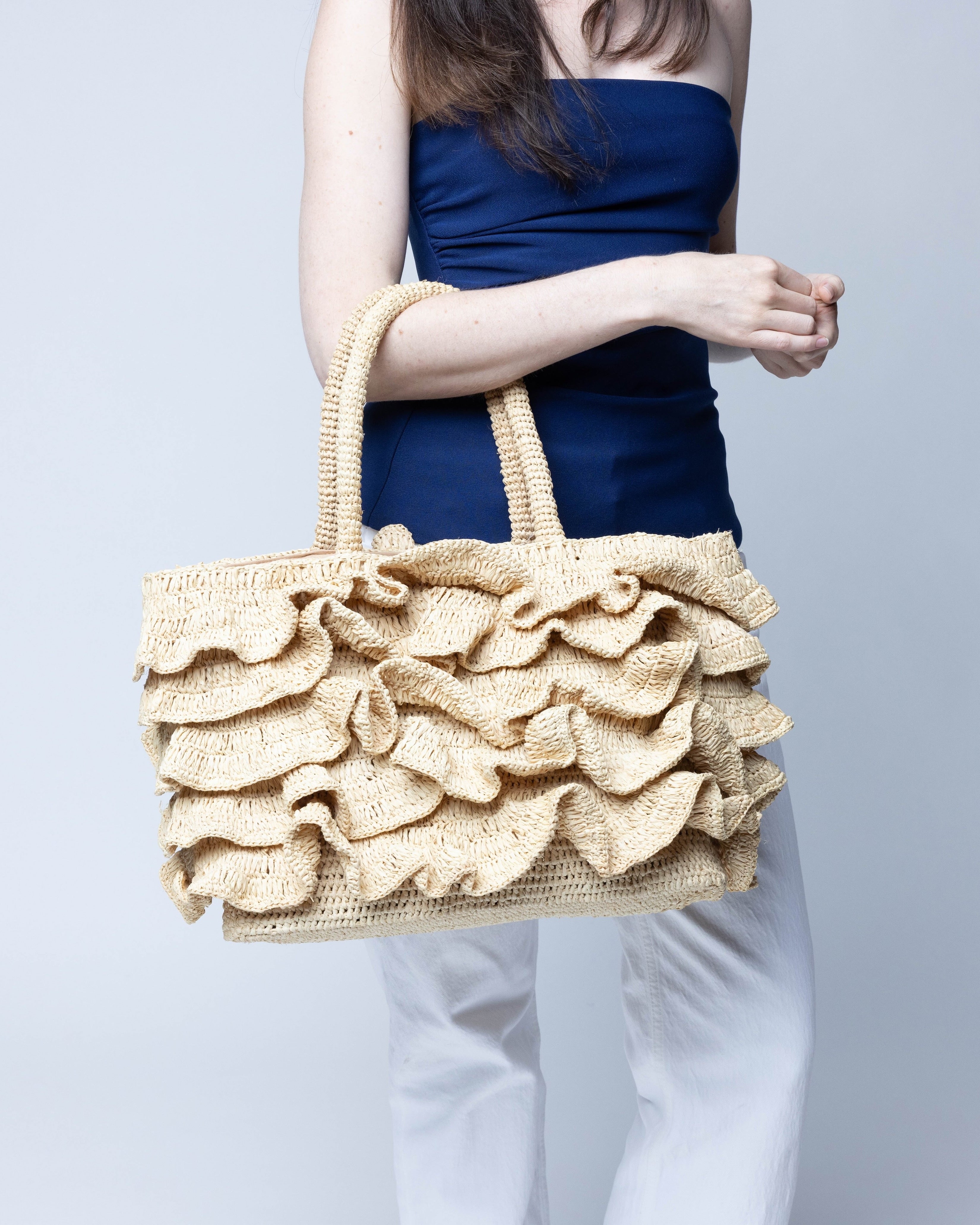 Model wearing Maryann Ruffle Crochet Straw Basket Handbag handmade crochet natural raffia palm fiber in a solid hue of natural straw color with generous eight tier ruffle horizontally layered around the circumference of the bag and banded link textured handles purse bag - Shebobo
