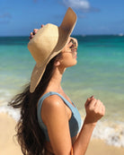 Model wearing Melanie 4.5" Wide Brim Raffia Straw Sun Hats handmade loomed natural raffia palm fiber in a solid hue of natural straw color round crown and flat brim with matching hatband and double bow detailing light weight breathable beach hat - Shebobo 