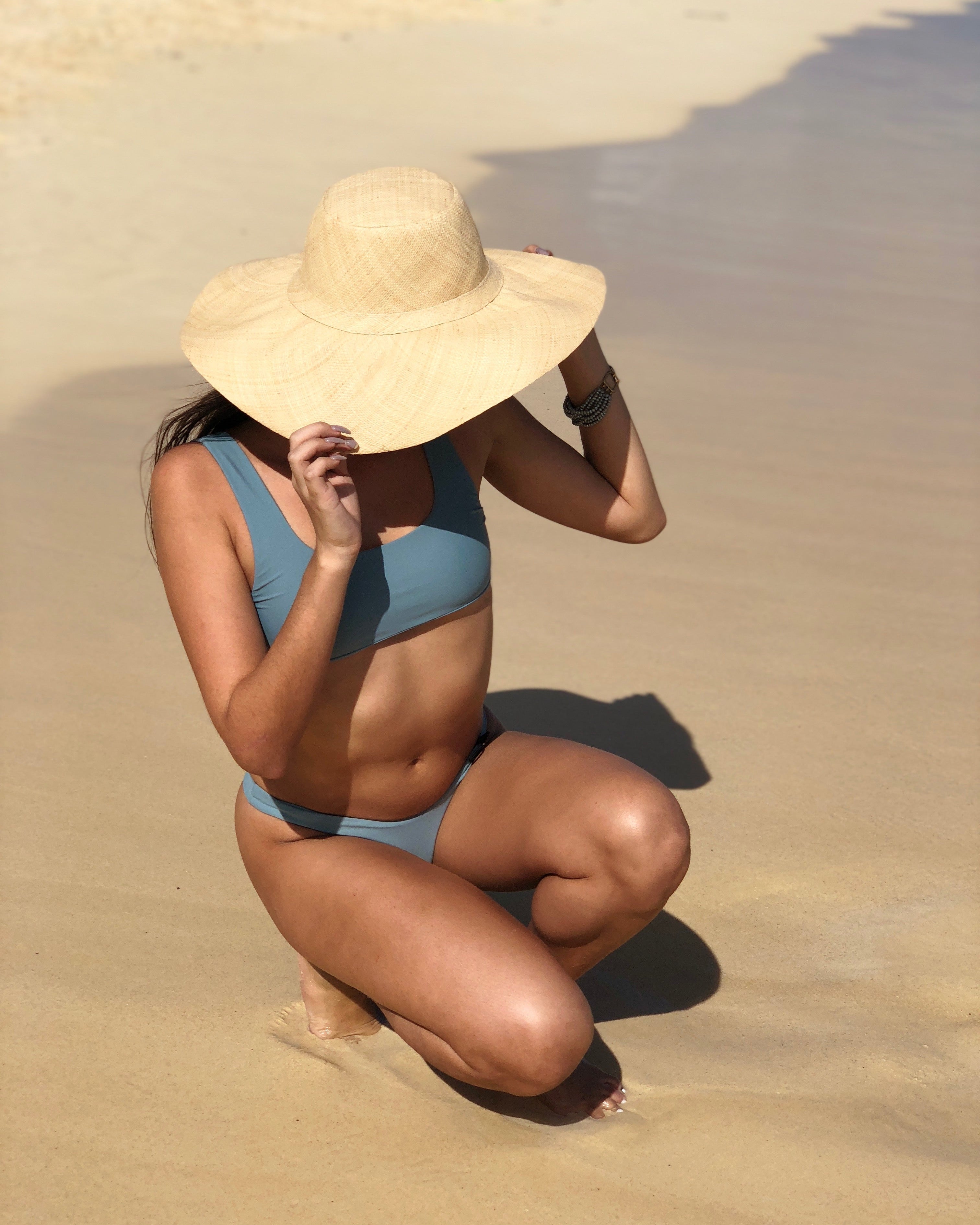 Model wearing Melanie 4.5" Wide Brim Raffia Straw Sun Hats handmade loomed natural raffia palm fiber in a solid hue of natural straw color round crown and flat brim with matching hatband and double bow detailing light weight breathable beach hat - Shebobo 