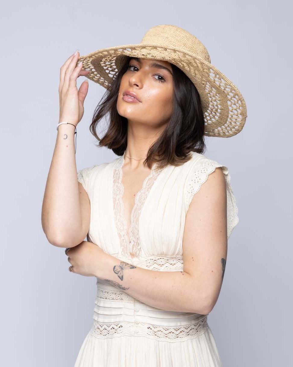 Model wearing Millie 4.5" Wide Brim Crochet Scallop Pattern Raffia Straw Sun Hat with Adjustable Wire Edge handmade woven natural raffia palm fiber in a solid hue of natural straw color with concentric spiral subtle link pattern starting on the top of the crown outwards with two circular bands of open scallop pattern weave on the brim separated by thicker bands of link texture with matching raffia braid hat band - Shebobo
