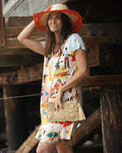 Model wearing Mimi handmade crochet granny square geometric square and floral pattern natural crochet crossbody bag straw purse with leather strap - Shebobo *dress by Kikisol with 5" Brim Vanessa Ombre Straw Sun Hat Coral and Natural handmade dip dye woven raffia with the color on the outer edge of the hat brim woven into natural as it progresses towards the inner brim with solid natural on the crown and detailed zig zag edging - Shebobo