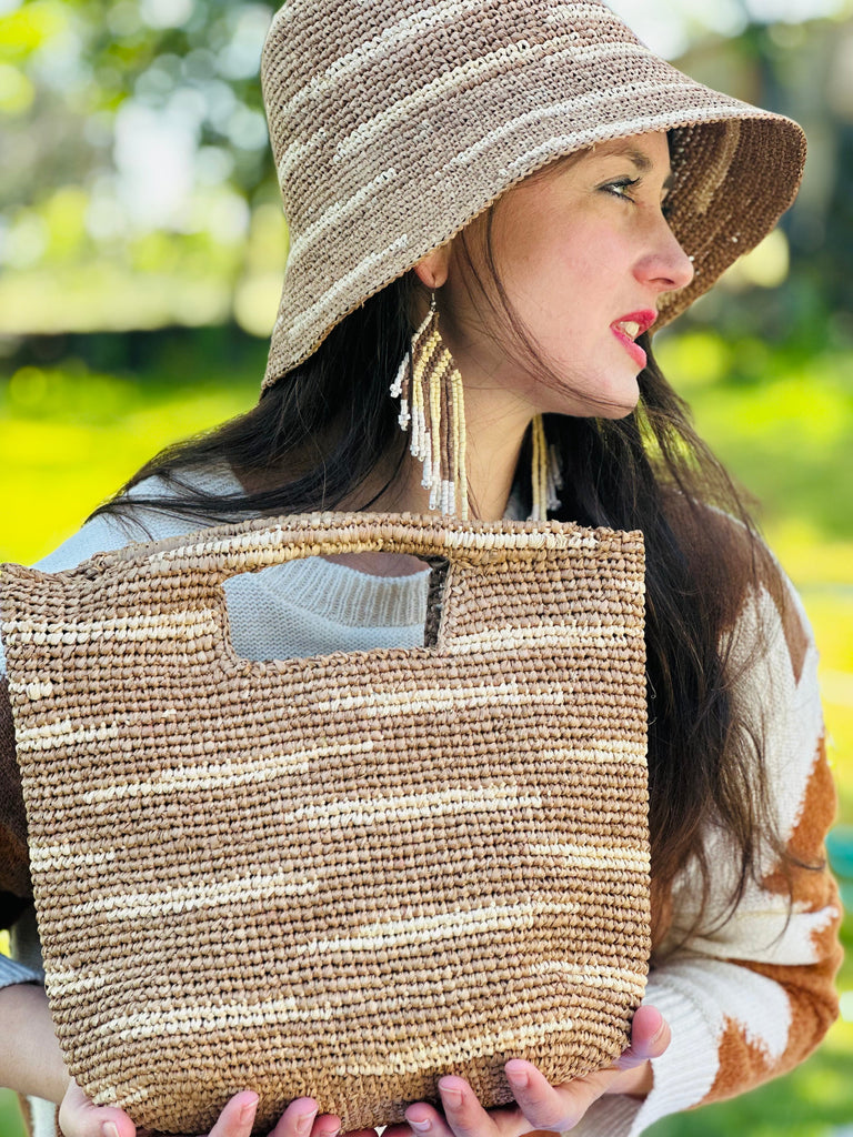 Model wearing Taylor Mini ConCon Crochet Cappuccino Straw Basket with Zebra Stripes handmade raffia palm fiber in a horizontal zebra stripe with short lengths of contrasting color in a dash pattern of cappuccino light brown with natural straw color accent petite handbag purse with matching Taylor Crochet Bucket Straw Hat - Shebobo