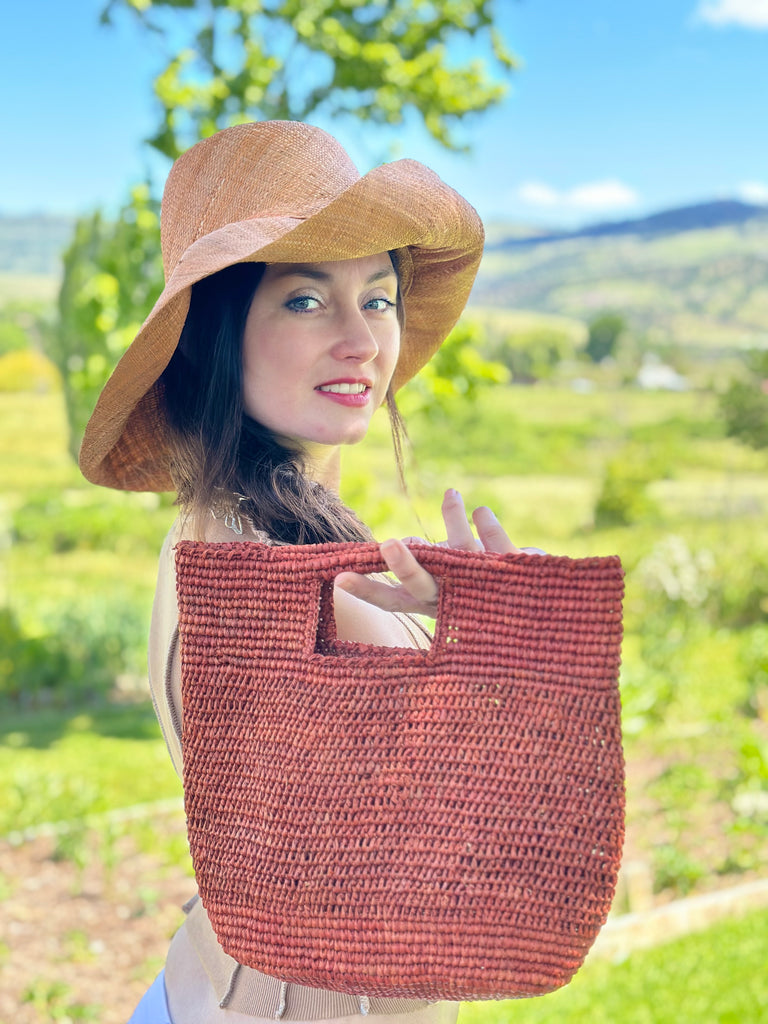 Model wearing 5" & 7" Wide Brim Solid Color Packable Straw Sun Hat handmade loomed raffia in a solid hue of blush pink/orange and Mini ConCon Crochet Petite Straw Basket Caramel - Shebobo