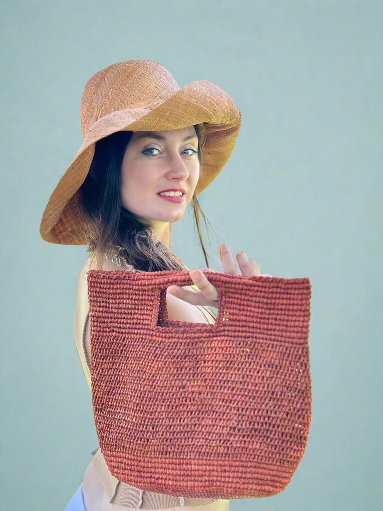 Model wearing Mini ConCon Whisky Crochet Petite Straw Basket Handmade natural raffia palm fiber crochet into a malleable basket bag of whisky deep red/brown hue handbag with 5" & 7" Brim Packable Solid Color Blush Straw Sun Hat - Shebobo