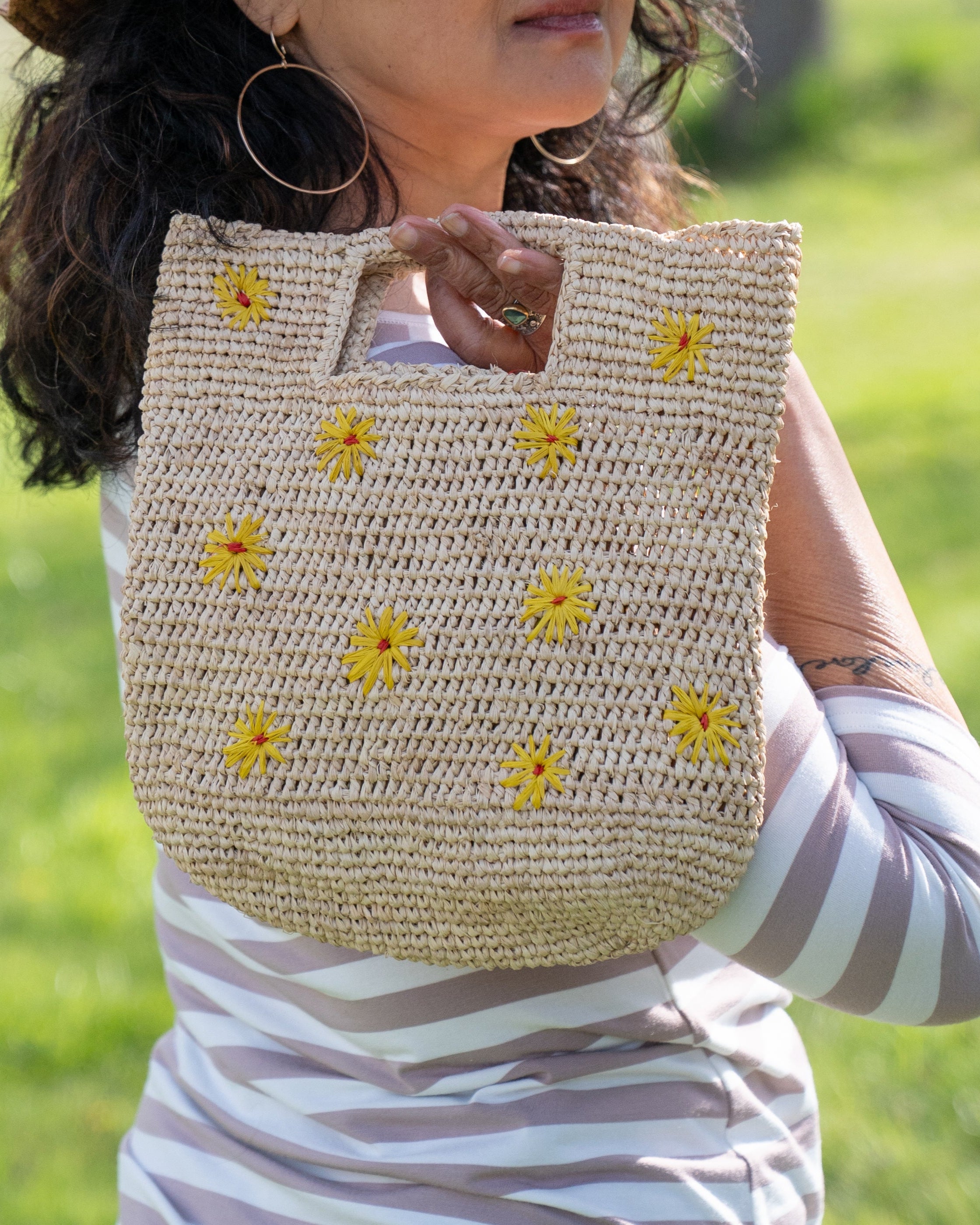 Model wearing Mini ConCon Flowers Crochet Petite Straw Basket handmade woven raffia palm fiber in a solid hue of natural straw color making a textured link pattern with delicate hand embroidered daisy floral pattern of saffron yellow with dot of coral orange/red in the center of each flower randomly placed around the entire bag handbag purse small bag - Shebobo