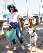 Model wearing Monica 7" Wide Brim Blue Swirl Multicolor Stripe Pattern Packable Straw Sun Hat handmade loomed raffia in multi width bands of navy blue, turquoise blue, and natural straw color create a striped swirl pattern - Shebobo (with Carmen Turquoise Straw Bucket Handbag with Bamboo Handles)