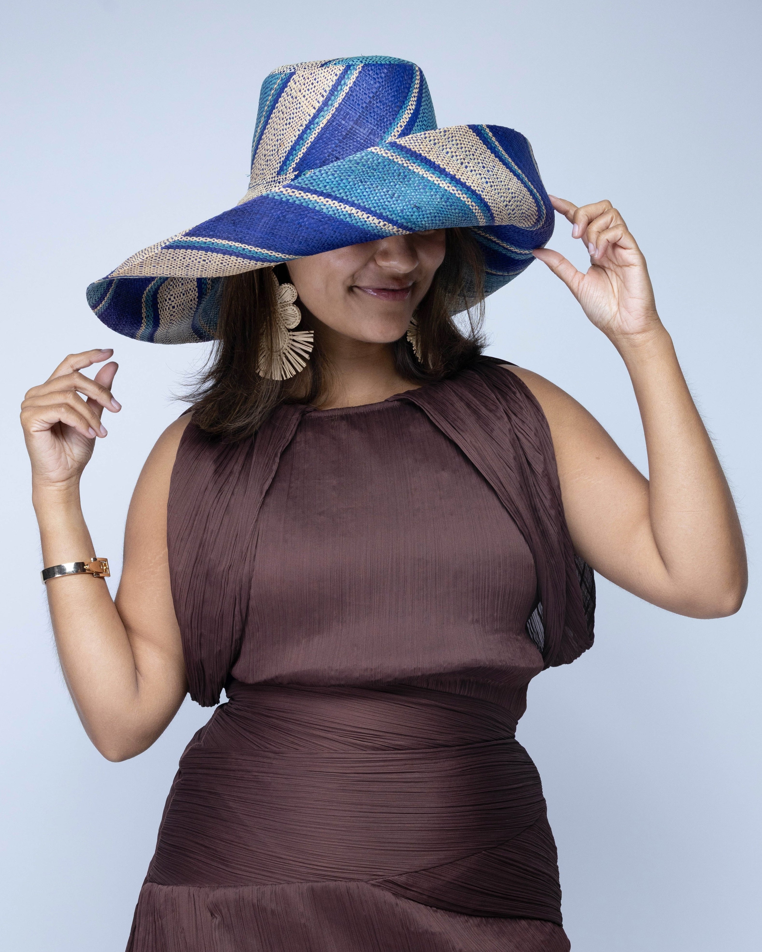 Model wearing Monica 7" Wide Brim Blue Swirl Multicolor Stripe Pattern Packable Straw Sun Hat handmade loomed raffia in multi width bands of navy blue, turquoise blue, and natural straw color create a striped swirl pattern - Shebobo