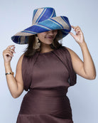 Model wearing Monica 7" Wide Brim Blue Swirl Multicolor Stripe Pattern Packable Straw Sun Hat handmade loomed raffia in multi width bands of navy blue, turquoise blue, and natural straw color create a striped swirl pattern - Shebobo