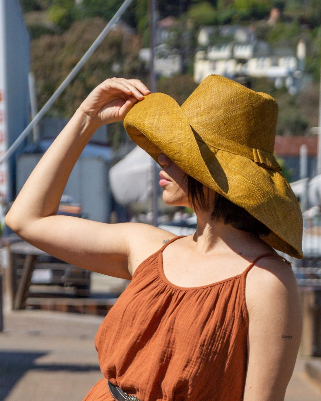 Model wearing Monica 7" Wide Brim Cinnamon Packable Straw Sun Hat handmade loomed natural raffia palm fiber in a solid hue of cinnamon/tobacco/brown - Shebobo