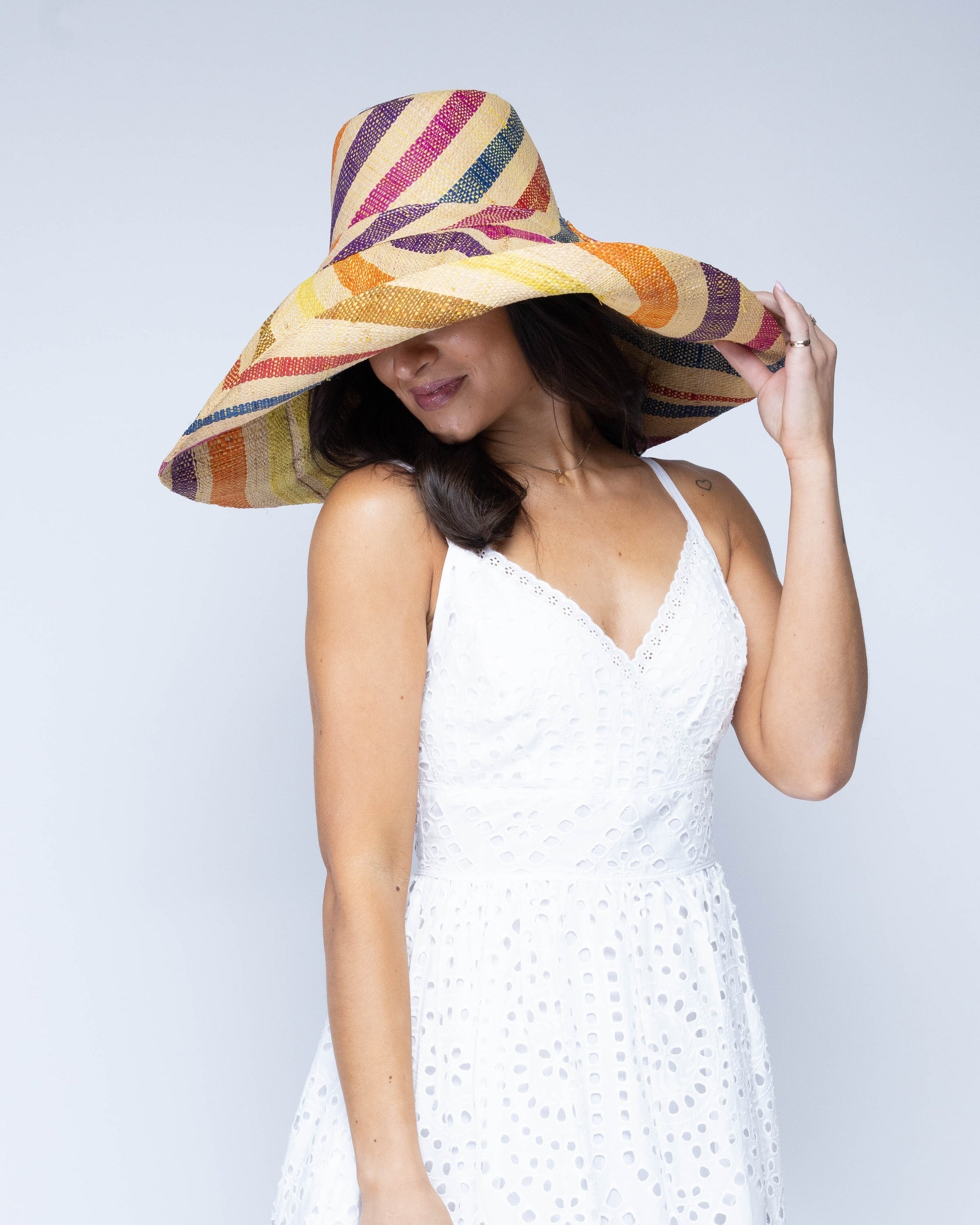 Model wearing Monica 7" Wide Brim Lingonberry Swirl Multicolor Stripes Packable Straw Sun Hat handmade loomed raffia in bands of natural straw color, red, purple, yellow, orange, turquoise blue, etc. stripes create a swirl pattern - Shebobo