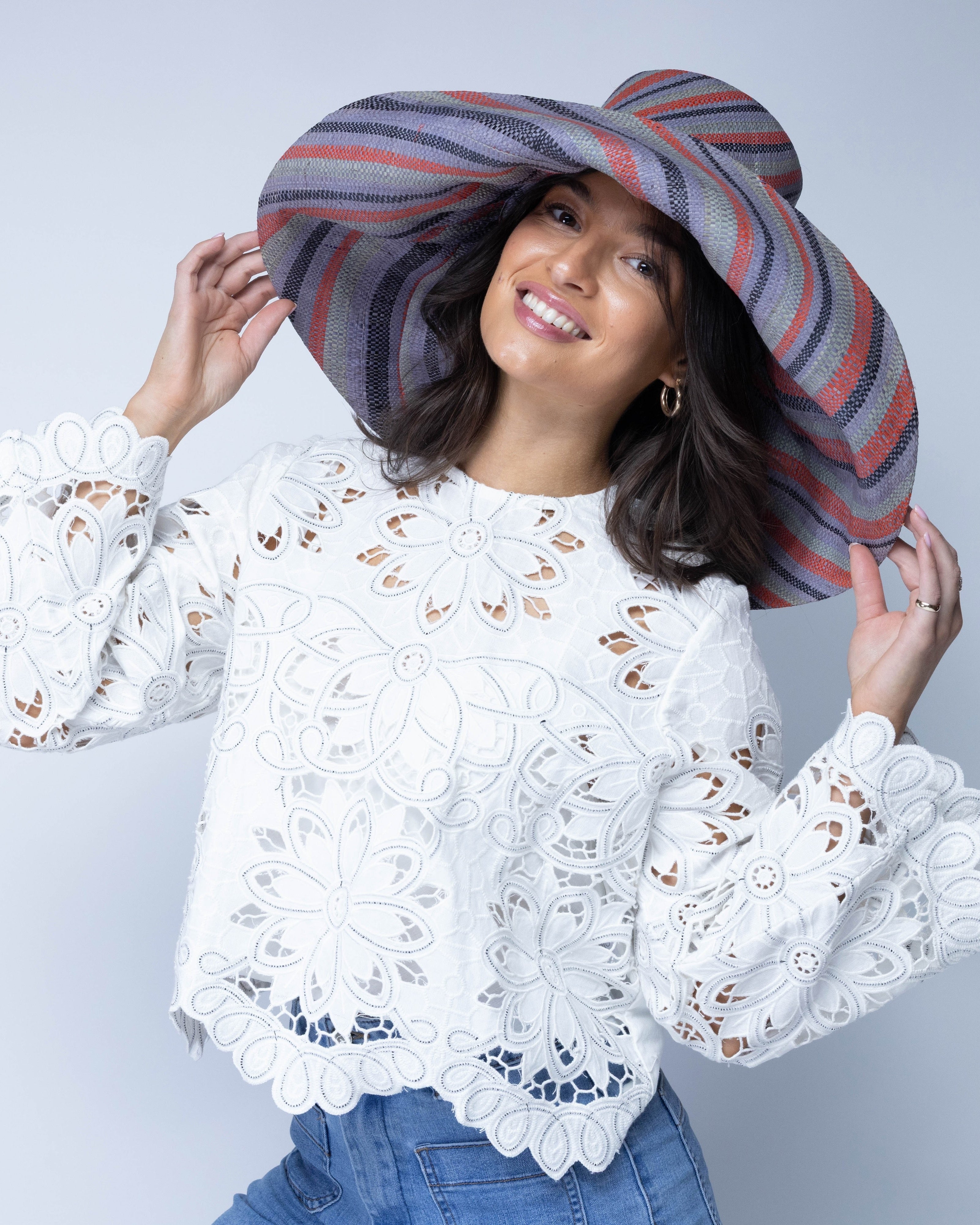 Model wearing Monica 7" Wide Brim Mulberry Swirl Multicolor Stripes Packable Straw Sun Hat handmade loomed raffia in bands of red, denim retro/light/blue, black, seafoam light/blue/green stripes create a swirl pattern - Shebobo
