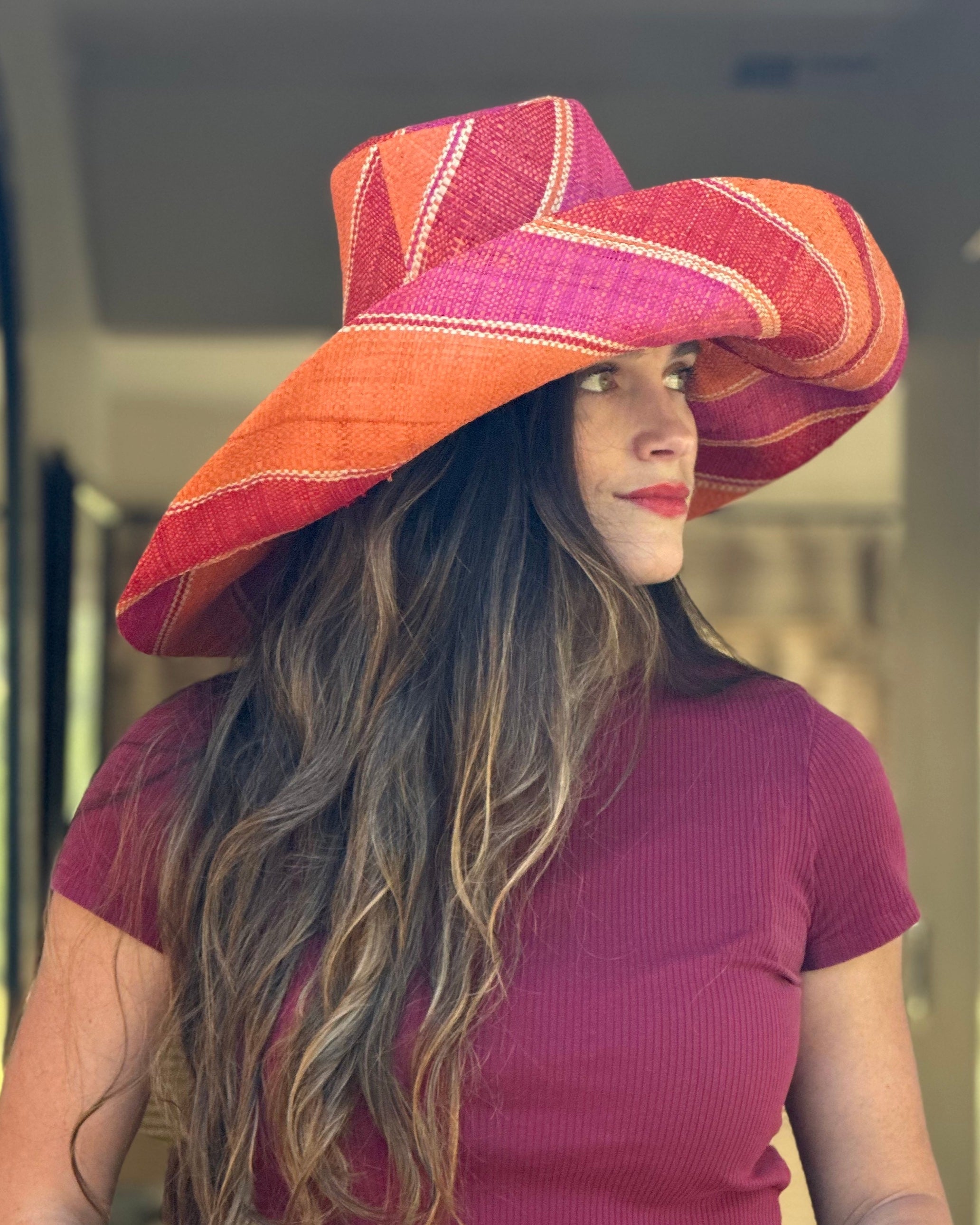 Model wearing Monica 7" Wide Brim Fuchsia & Coral Swirl Multicolor Stripes Packable Straw Sun Hat Handmade loomed raffia in multi width bands of fuchsia pink, coral orange, red, and natural straw color create a swirl pattern - Shebobo