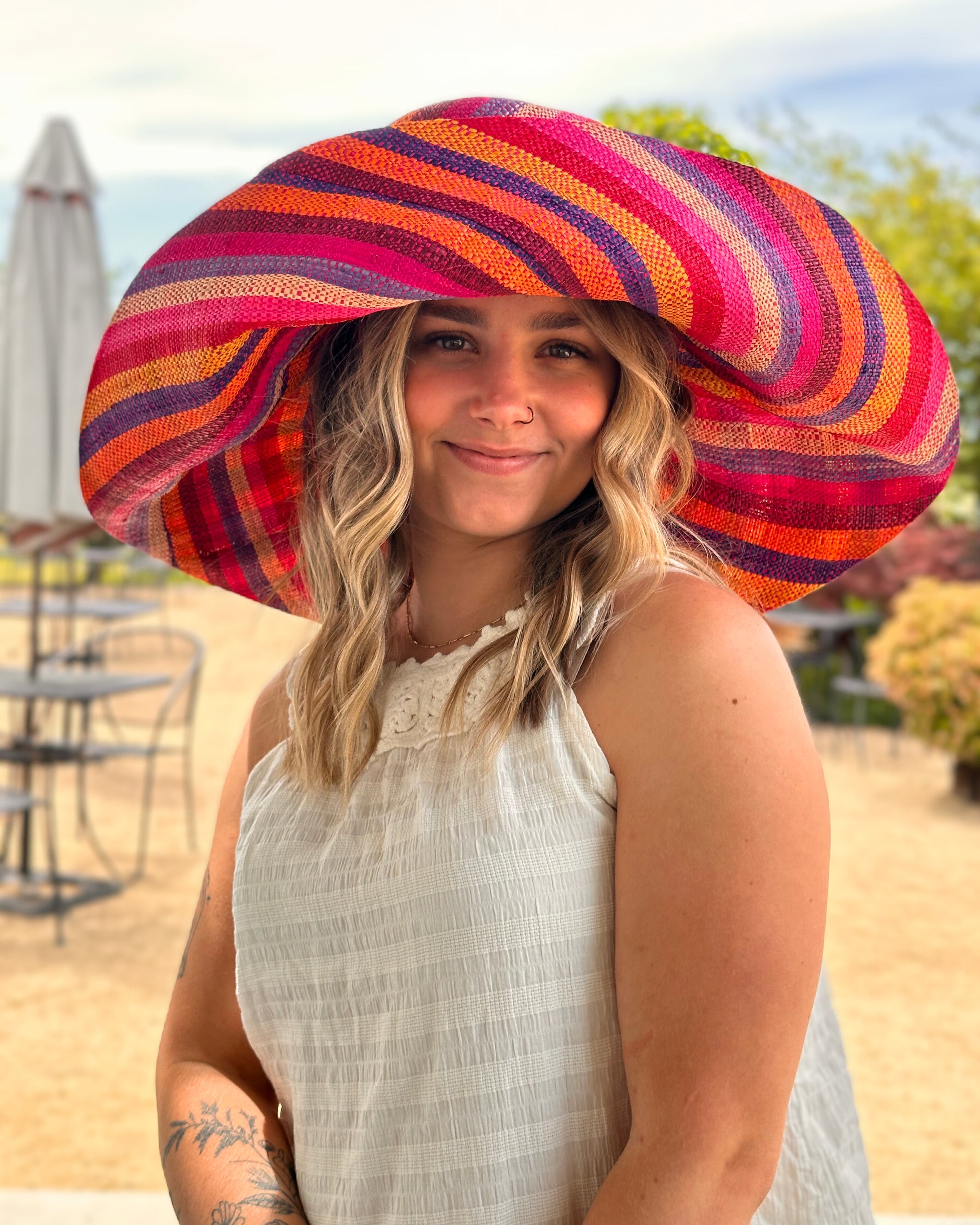 Model wearing Monica 7" Wide Fiesta Stripe Multicolor Stripes Packable Straw Sun Hat Handmade loomed raffia multi width bands of fuchsia pink, bordeaux red, saffron yellow, coral orange, natural straw color, purple, blue, etc. create a swirl pattern - Shebobo