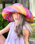 Model wearing Monica 7" Wide Brim Midori Swirl Multicolor Stripes Packable Straw Sun Hat Handmade loomed raffia in multi width bands of orange, lime green, fuchsia pink, purple, etc. create a swirl pattern - Shebobo