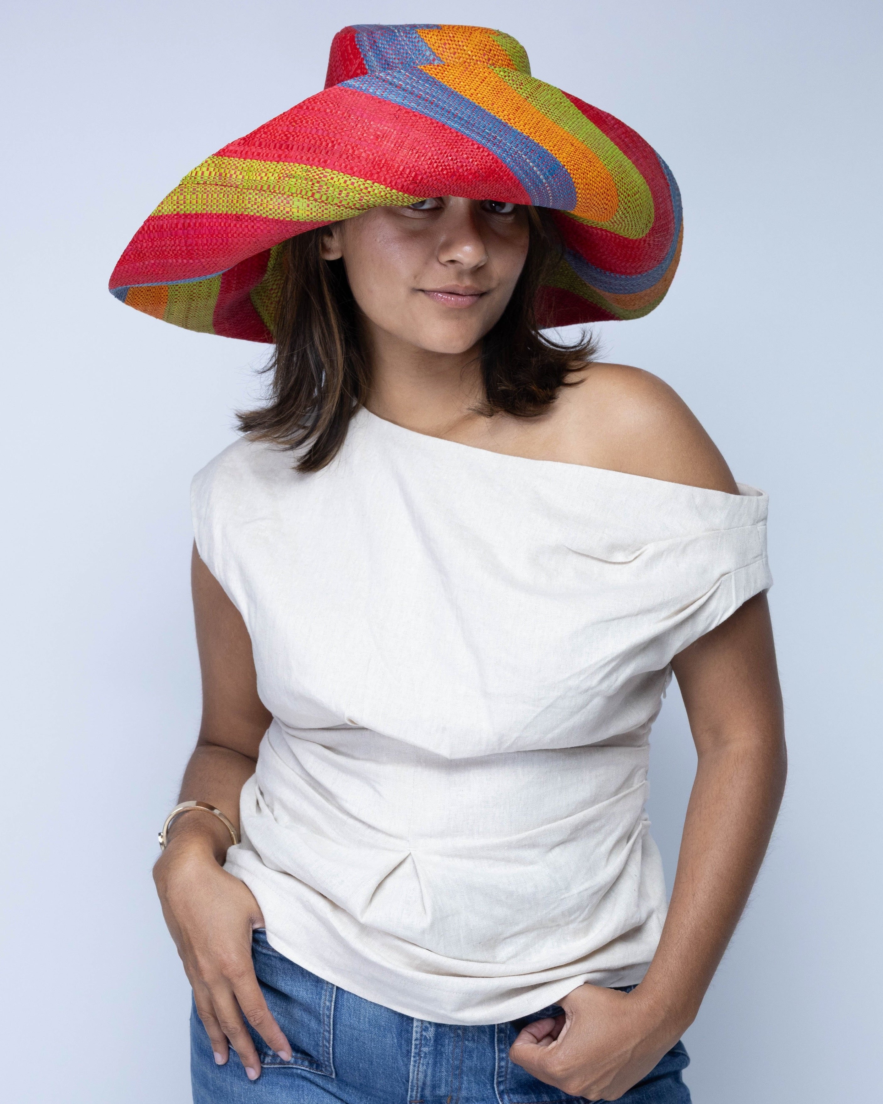 Model wearing Monica 7" Wide Brim Na Pali Swirl Multicolor Stripes Packable Straw Sun Hat handmade loomed raffia in bands of red, saffron yellow/orange, midori lime/green, and denim retro/light/blue stripes create a swirl pattern - Shebobo
