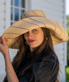 Model wearing Monica 7" wide brim natural and Neutrals multicolor pinstripes packable raffia straw hat handmade loomed raffia in wide bands of natural straw color with narrow bands of blush orange/pink, cinnamon/tobacco/brown, black, and grey create a stripe swirl pattern - Shebobo