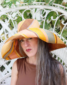 Model wearing Monica 7" Wide Brim Pink Blue Swirl Multicolor Stripes Packable Straw Sun Hat Handmade loomed raffia in multi width bands of saffron yellow, light pink, light blue, black, natural straw color etc. create a swirl pattern - Shebobo