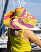 Model wearing Monica 7" Wide Brim Pink Lemonade Swirl Multicolor Stripes Packable Straw Sun Hat Handmade loomed raffia in multi width bands of fuchsia pink, purple, yellow, midori lime/green, and natural straw color create a swirl pattern - Shebobo