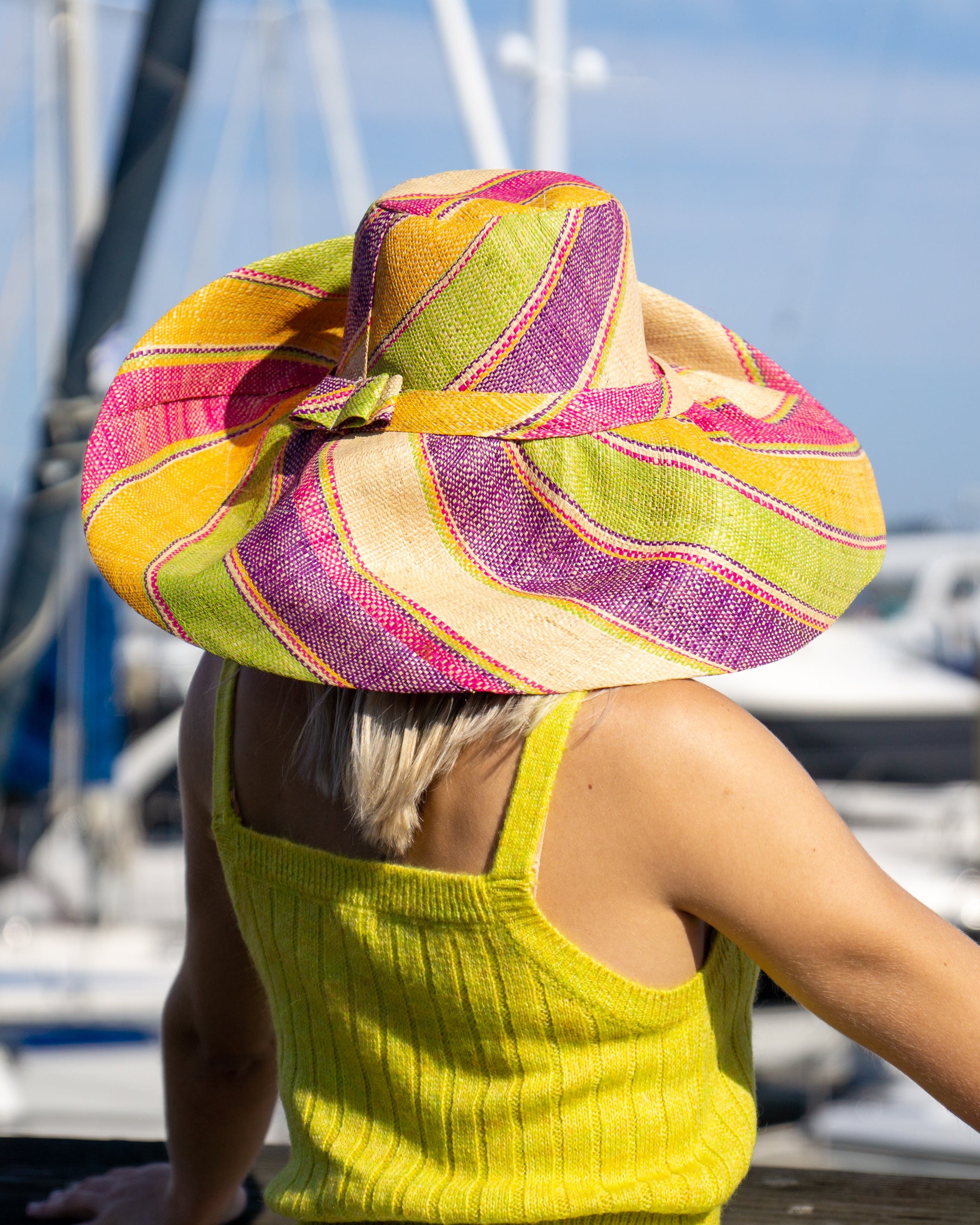 Model wearing Monica 7" Wide Brim Pink Lemonade Swirl Multicolor Stripes Packable Straw Sun Hat Handmade loomed raffia in multi width bands of fuchsia pink, purple, yellow, midori lime/green, and natural straw color create a swirl pattern - Shebobo