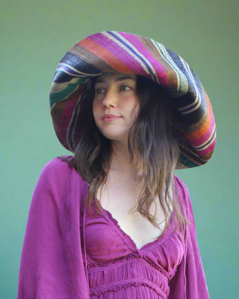 Model wearing Monica  7" Wide Brim Revel Swirl Multicolor Stripes Packable Straw Sun Hat Handmade loomed raffia in multi width bands of coral orange, fuchsia pink, teal blue/green, purple, cinnamon/tobacco/brown, black, natural straw color etc. create a swirl pattern - Shebobo