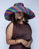 Model wearing Monica 7" Wide Brim Riviera Swirl Multicolor Stripes Packable Straw Sun Hat handmade loomed raffia in bands of fuchsia hot/bright/pink, purple, coral orange/red, midori lime/green, and turquoise blue stripes create a swirl pattern - Shebobo