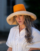 Model wearing Monica 7" Brim Two Tone Saffron Straw Hat handmade loomed raffia color block pattern of the top half saffron orange/yellow and the bottom half natural straw color - Shebobo