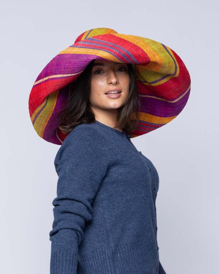 Model wearing Monica 5" & 7" Wide Brim Sangria Swirl Multicolor Stripes Packable Straw Sun Hat Handmade loomed raffia in multi width bands of red, purple, midori lime/green, turquoise blue, saffron yellow/orange, natural straw color, etc. create a swirl pattern - Shebobo
