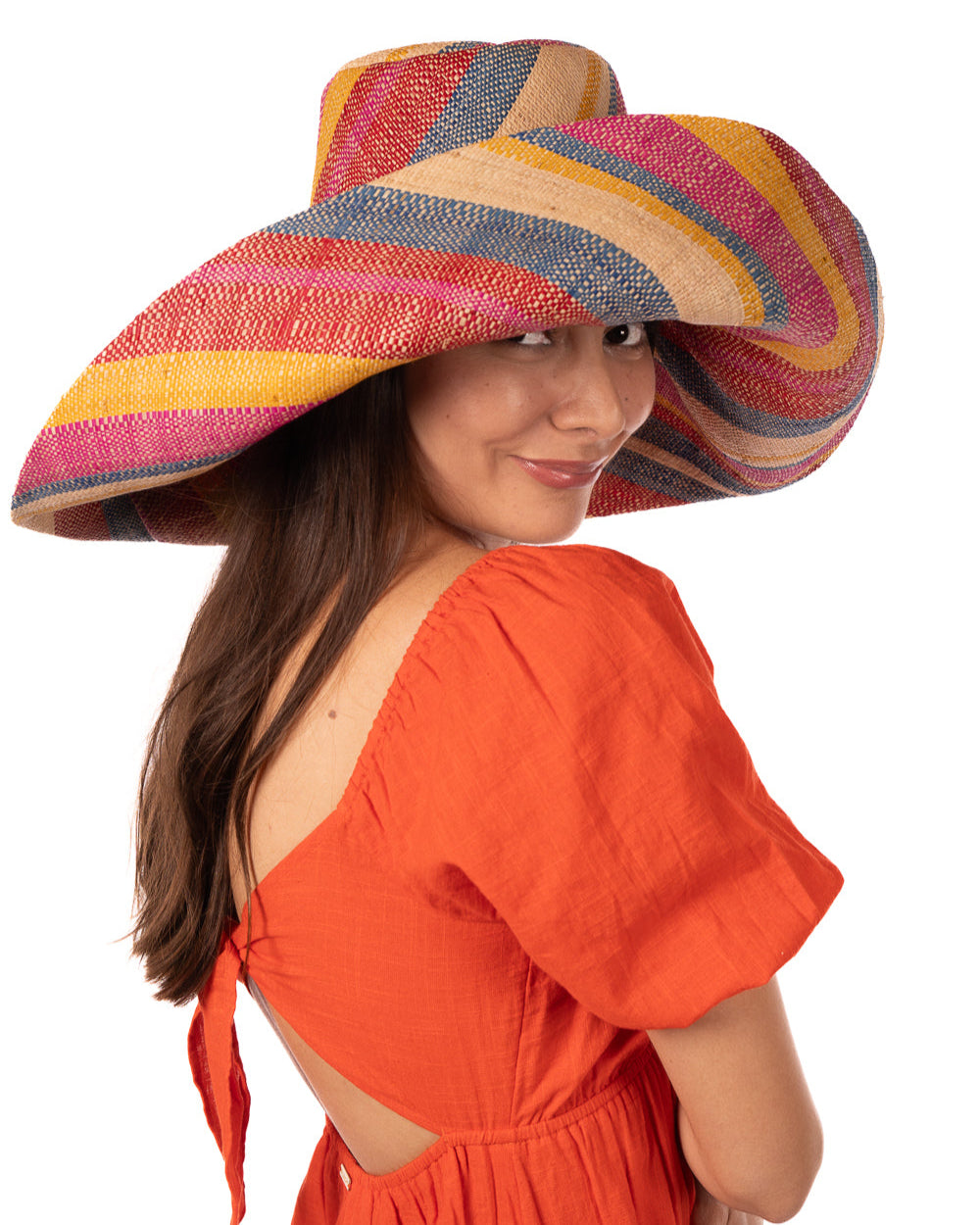 Model wearing Monica 7" Wide Brim Sassafras Swirl Multicolor Stripes Packable Straw Sun Hat Handmade loomed raffia in multi width bands of fuchsia pink, red, saffron yellow, navy blue, and natural straw color create a swirl pattern - Shebobo