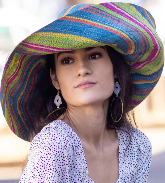 Model wearing  7" Wide Brim Turquoise and Lime Multicolor Stripes Packable Straw Sun Hat Handmade loomed raffia multi width bands of turquoise blue, lime green, fuchsia pink, orange, yellow, and natural straw color create a swirl pattern - Shebobo