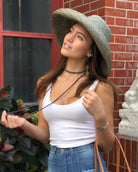 Model wearing Monica 5" Wide Brim Solid Color Packable Straw Sun Hat handmade loomed raffia in a solid hue of pewter light/grey - Shebobo