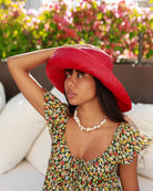 Model wearing Monica 5" Wide Brim Red Packable Straw Sun Hat handmade loomed raffia in a solid hue of red lightweight malleable flexible sun protection hat - Shebobo