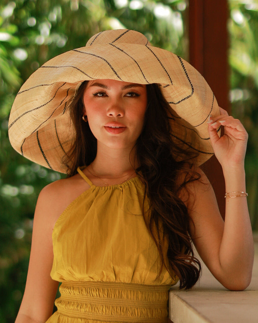 Model wearing Monica 7" wide brim natural and black pinstripes packable raffia straw hat handmade loomed raffia in wide bands of natural straw color with black narrow bands create a stripe swirl pattern - Shebobo