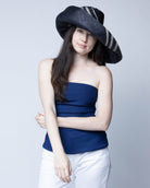 Model wearing Monica 7" Wide Brim Racing Stripe Packable Straw Sun Hats handmade loomed natural raffia palm fiber in a solid hue of black with a three stripe racing stripe pinstripe pattern of natural straw color that creates a swirl around the crown and brim of the hat lightweight breathable sun protection - Shebobo