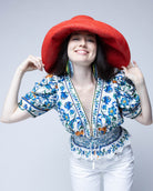 Model wearing Monica 7" Wide Brim Coral Solid Color Packable Straw Sun Hat handmade loomed raffia in a solid hue of coral orange/red  - Shebobo