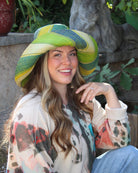 Model wearing Monica 5" Wide Brim Izarra Swirl Multicolor Stripes Packable Straw Sun Hat Handmade loomed raffia in multi width bands of midori lime/green, teal, dusk navy/dark/blue, yellow, natural straw color etc. create a swirl pattern - Shebobo