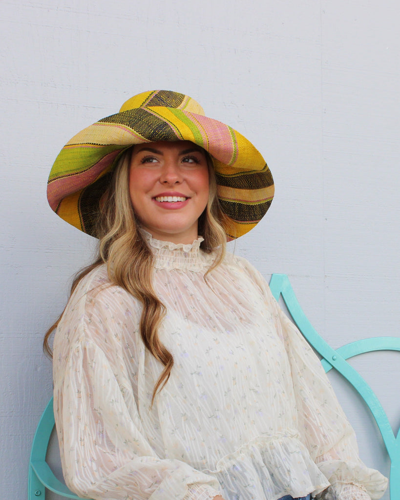 Model wearing Monica 5" Wide Brim Lemonade Swirl Multicolor Stripes Packable Straw Sun Hat Handmade loomed raffia in multi width bands of yellow, wisteria light/purple/pink, midori lime/green, black, natural straw color etc. create a swirl pattern - Shebobo