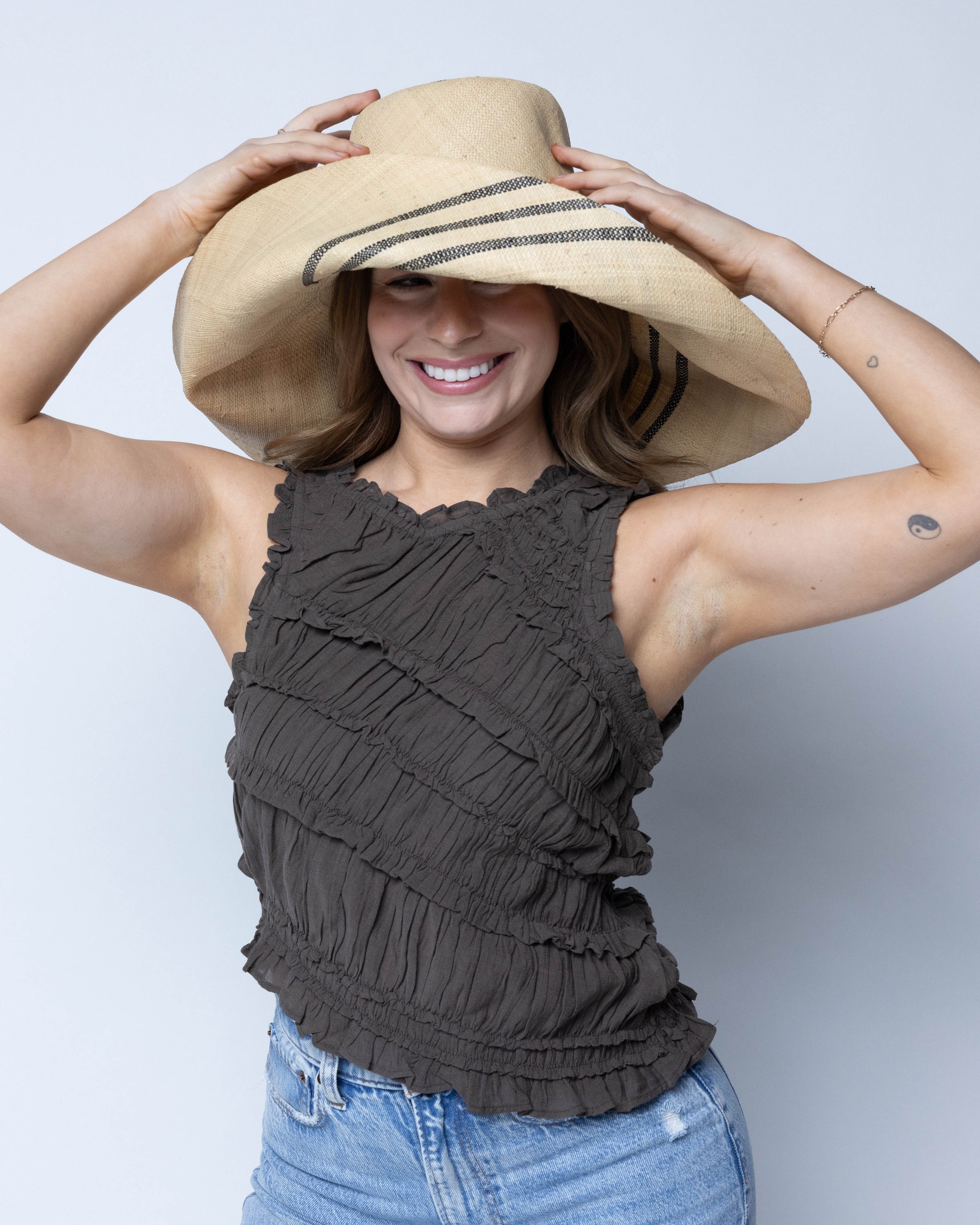 Model wearing Monica 5" & 7" Wide Brim Racing Stripe Packable Straw Sun Hats handmade loomed natural raffia palm fiber in a solid hue of natural straw color with a black three stripe racing stripe pinstripe pattern that creates a swirl around the crown and brim of the hat lightweight breathable sun protection - Shebobo