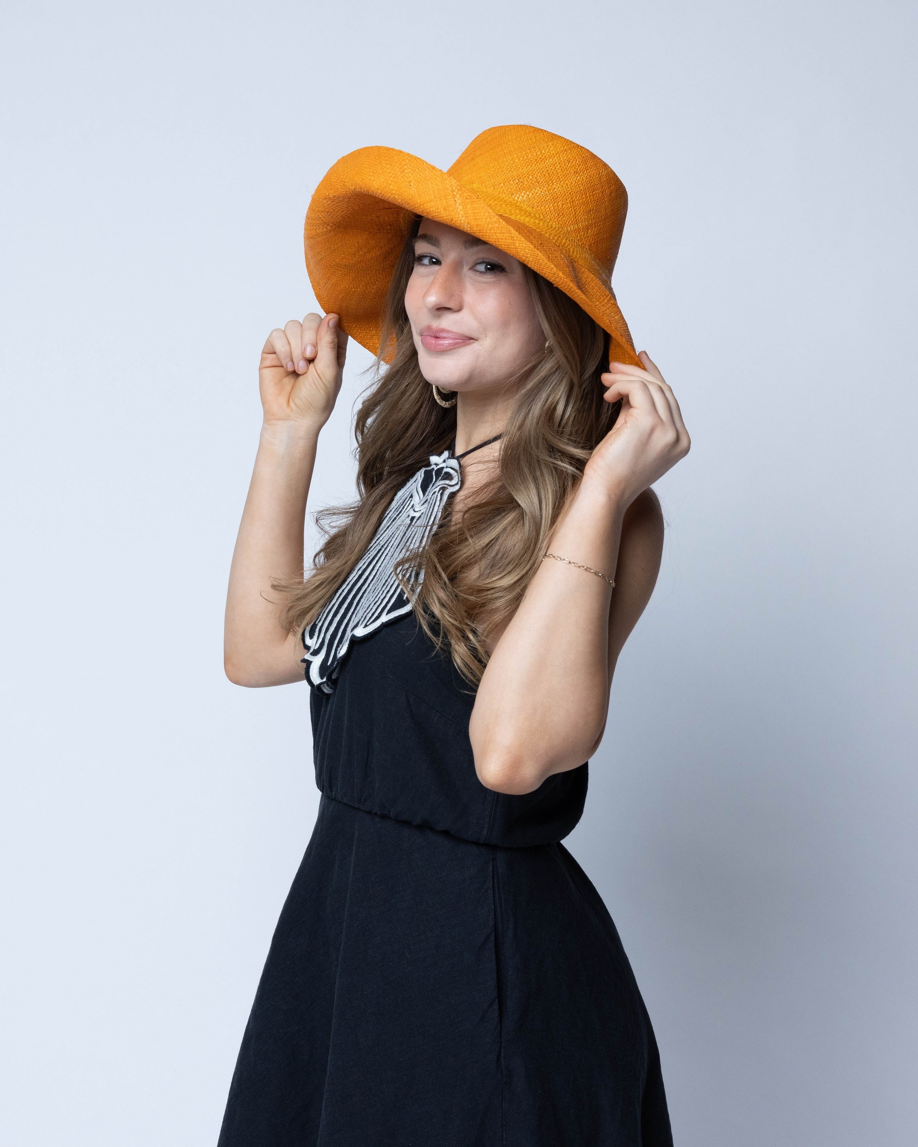 Model wearing Monica 5" Wide Brim Saffron Packable Straw Sun Hat handmade loomed raffia in a solid hue of saffron yellow/orange lightweight malleable flexible hat - Shebobo